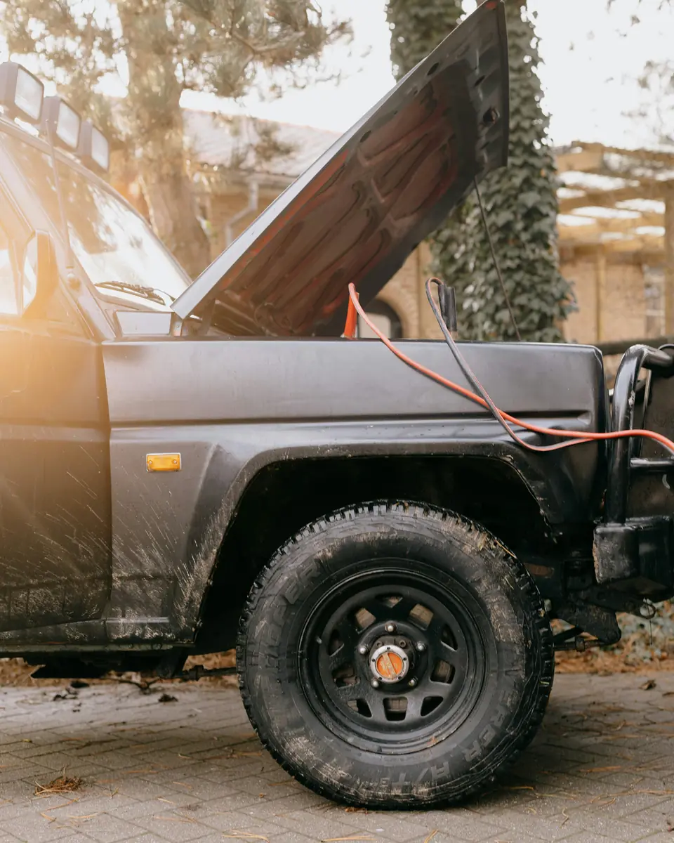 A 4x4 with its bonnet up and jump leads attached, parked on a block-paved driveway