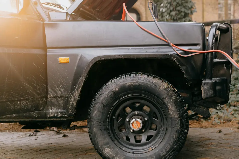 A 4x4 with its bonnet up and jump leads attached on a driveway